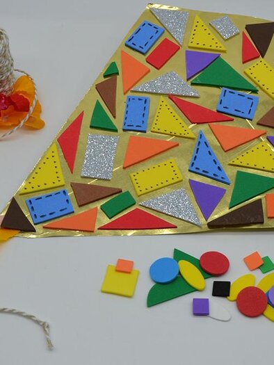 A colorful handcrafted kite with various shapes and colors lies on a table. Next to the kite, craft materials and gift ribbon can be seen. | ©  KulturQuartier Leoben