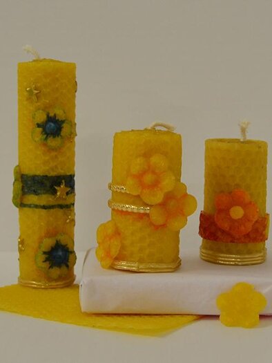 Three decorative yellow candles with floral patterns are placed on a white background. Next to the candles lies a yellow sheet of wax. | © KulturQuartier Leoben