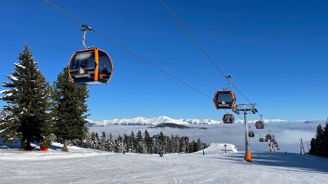 Eine Skilandschaft mit Sesselliften und verschneiten Bäumen. Im Hintergrund sind Berge und ein klarer Himmel zu sehen.