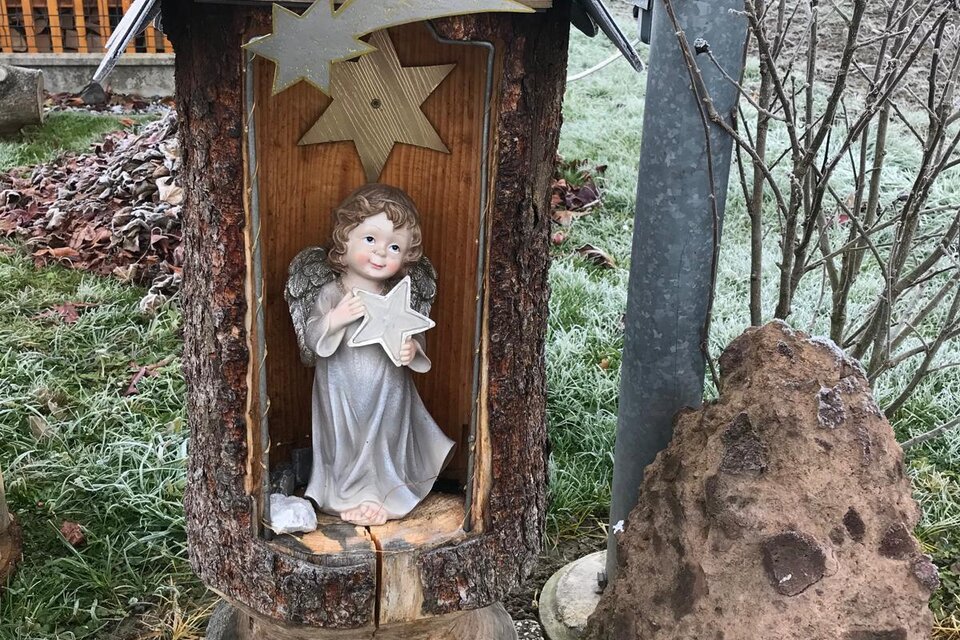 Eine dekorative Figur eines Engels sitzt in einem hölzernen Stall mit einem Dach. Umgeben von der Natur zeigt das Bild eine rustikale, weihnachtliche Atmosphäre. | © Marktgemeinde Halbenrain
