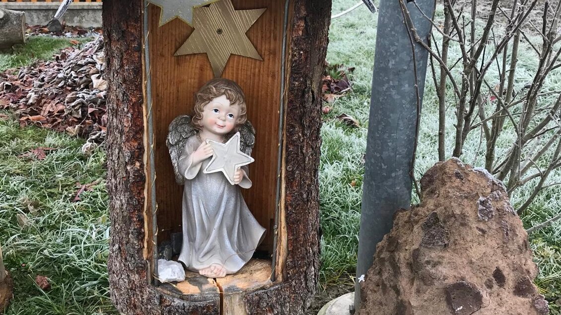 Eine dekorative Figur eines Engels sitzt in einem hölzernen Stall mit einem Dach. Umgeben von der Natur zeigt das Bild eine rustikale, weihnachtliche Atmosphäre. | © Marktgemeinde Halbenrain