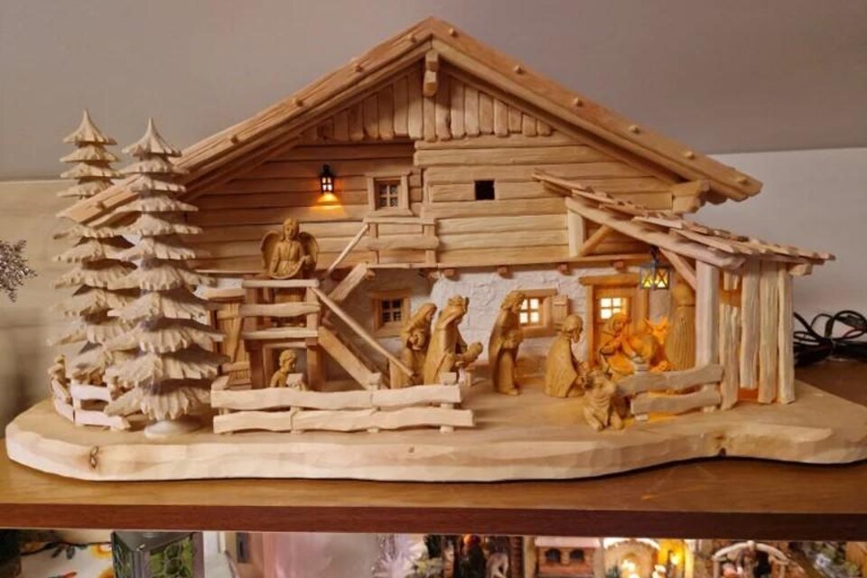 Eine dekorative Holzfigur eines ländlichen Gebäudes mit Figuren und Bäumen. Das Modell zeigt eine liebevoll gestaltete Szene im alpinen Stil. | © Adi Barazutti