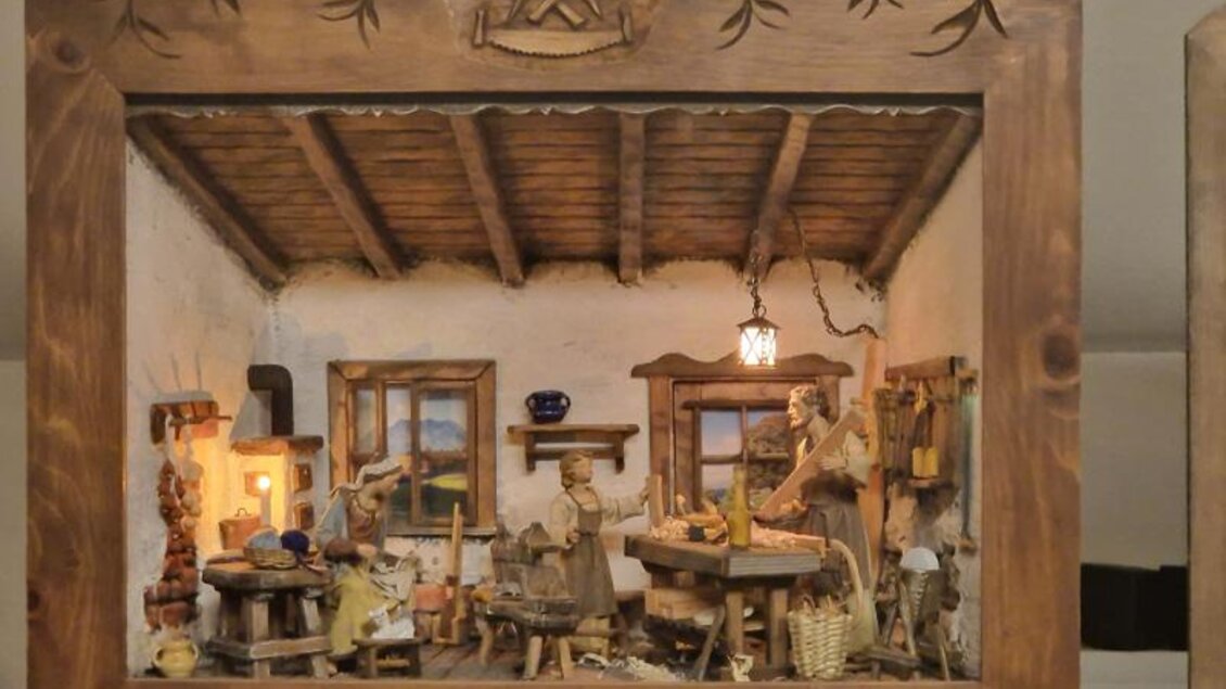 Eine detaillierte Schaukästen-Szene mit einem rustikalen Tisch und Figuren, die in einem gemütlichen Raum mit Holzbalkendecke arbeiten. Die Atmosphäre ist traditionell und einladend, mit warmem Licht und handwerklichen Details. | © Adi Barazutti