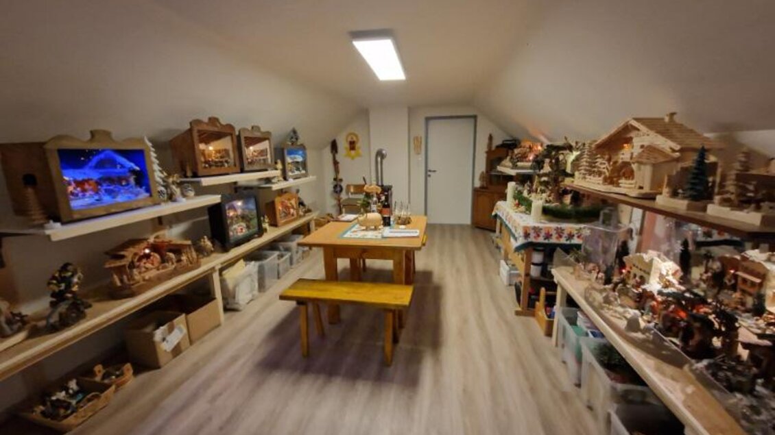 Ein gemütlicher Raum mit Holzmöbeln und vielen dekorativen Objekten. In der Mitte steht ein Tisch mit einer Holzbank, umgeben von Regalen mit verschiedenen Sammlerstücken. | © Adi Barazutti