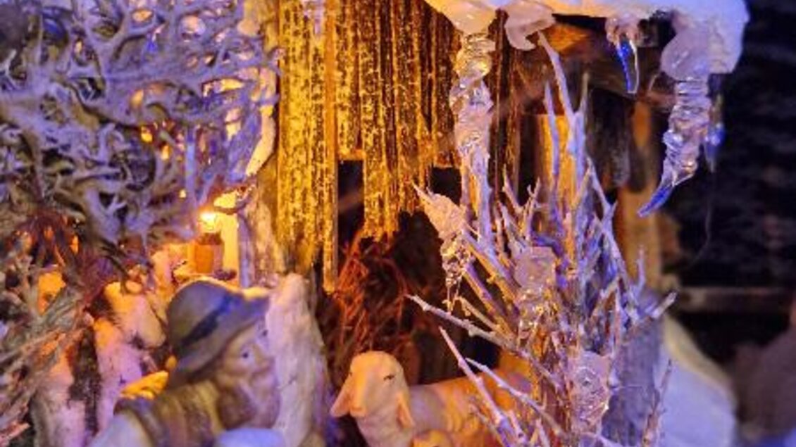 Eine winterliche Szene mit einer Schneelandschaft und einer kleinen Hütte. Eine Figur trägt ein Schaf, während in der Nähe Tiere stehen und Eiszapfen von der Hütte hängen. | © Adi Barazutti