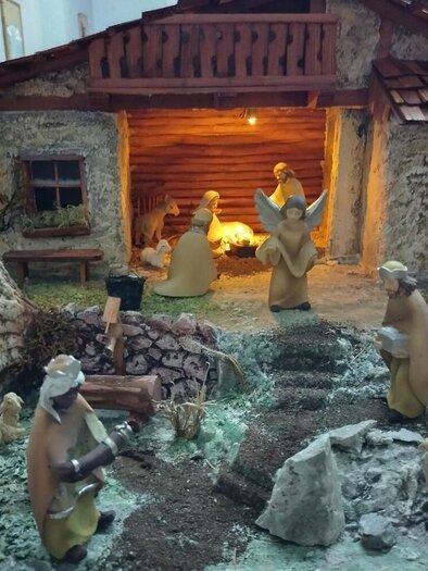 A traditional nativity scene with figures gathered around a stable. In the background, there is a cozy fire and the landscape is decorated with stones and small animals. | © Krippenverein St. Anna am Aigen