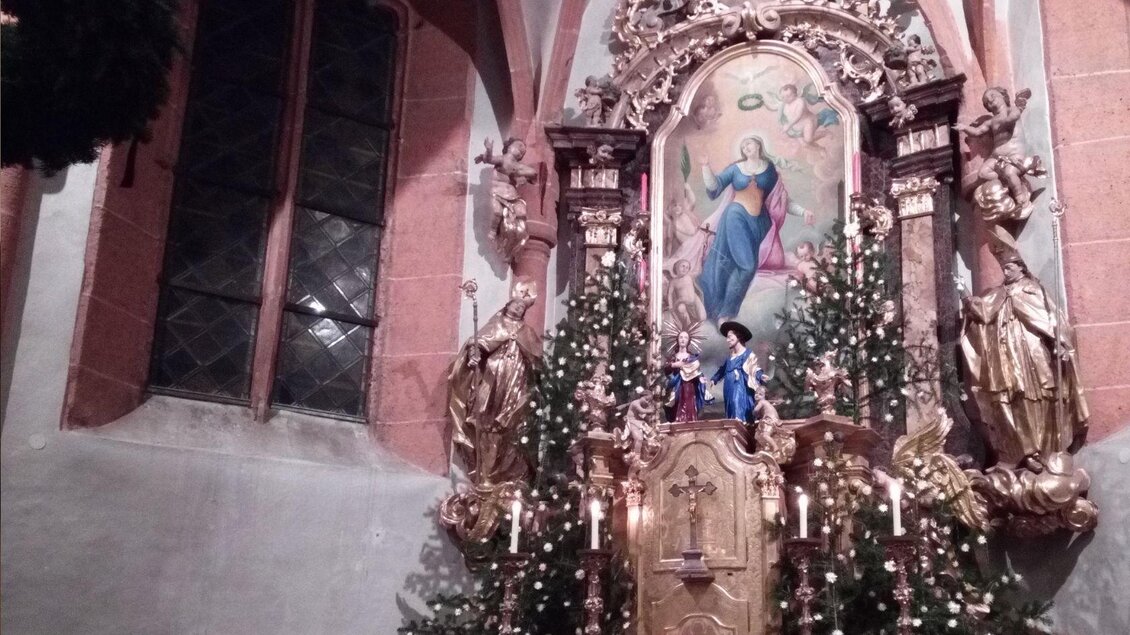 Ein dekorierter Altar in einer Kirche, umgeben von Tannen und Kerzen. Im Hintergrund ist ein religiöses Gemälde mit der Darstellung einer heiligen Figur zu sehen. | © TVB Ausseerland Salzkammergut