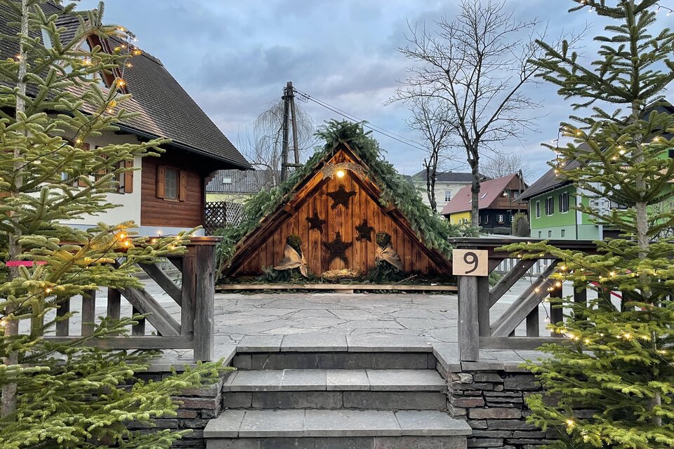 Eine gemütliche Hütte aus Holz mit grünen Tannenzweigen auf dem Dach steht im Vordergrund. Besondere Weihnachtsdekorationen und umgebende Tannen sorgen für eine festliche Atmosphäre. | © TV Südsteiermark