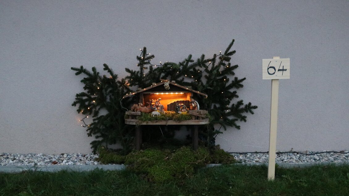 Eine kleine Weihnachtskrippe mit einer stimmungsvollen Beleuchtung steht vor einem grauen Hintergrund. Daneben steht ein Schild mit der Nummer 64. | © TV Südsteiermark