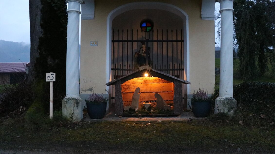 Eine kleine Kapelle mit einem beleuchteten Innenraum. Vor der Kapelle stehen Blumentöpfe und eine Nummerierung auf der linken Seite. | © TV Südsteiermark