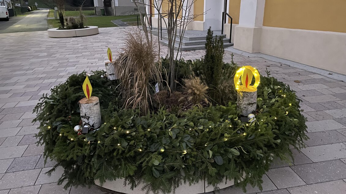 Ein dekorierter Pflanzenschmuck mit einer Vielzahl von grünen Pflanzen und zwei leuchtenden Kerzen. Der Bereich ist festlich und einladend gestaltet. | © TV Südsteiermark