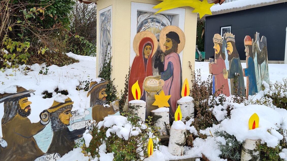 Eine festliche Weihnachtskrippe im Schnee mit Figuren und einer kleinen Hütte. Umgeben von geschneiten Pflanzen und dekorativen Kerzen. | © Robier Johann| „Kripperlroas Oberhaag“