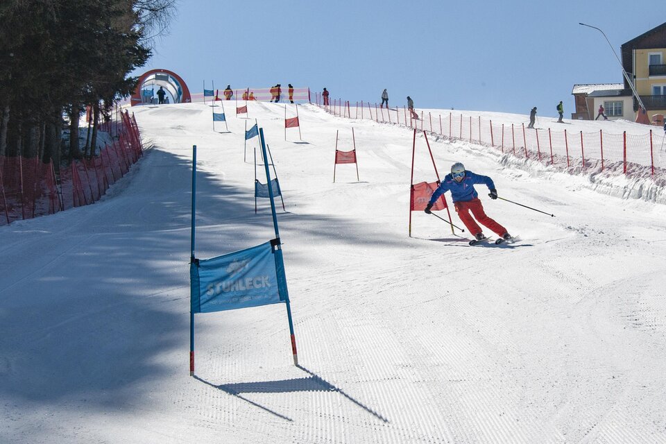 Auf dem Foto sieht man eine Skipiste, auf der ein Skirennfahrer einen Riesentorlauf mit roten und blauen Fahnenstangen fährt. | © Hannes Gsell
