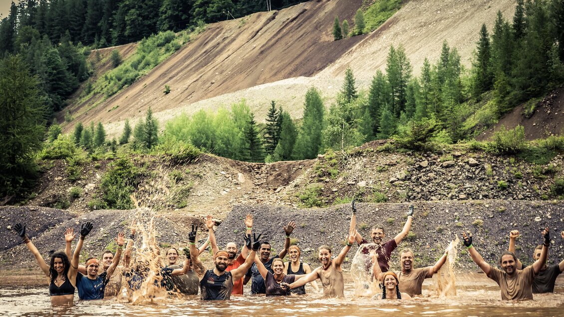 Eine Gruppe von Menschen steht in einem Gewässer und erfreut sich am Schwimmen. Sie lachen und posieren, während sie mit den Händen Wasser spritzen. | © Sportfotograf Tiqa