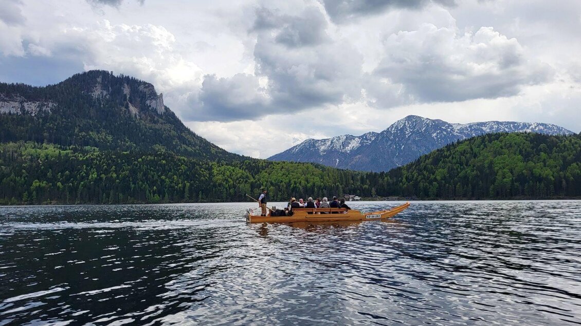 Ein Boot mit mehreren Personen fährt auf einem ruhigen See. Im Hintergrund sind majestätische Berge und eine bewaldete Landschaft zu sehen. | © TVB Ausseerland Petra Kirchschlager