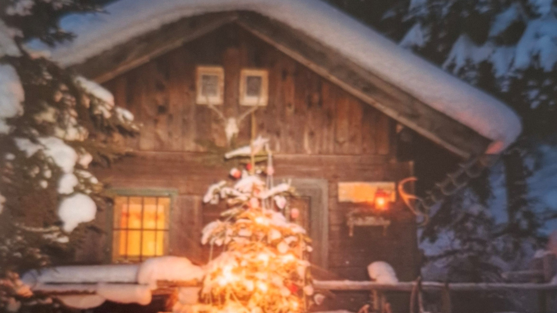 Eine gemütliche Berghütte im Schnee, beleuchtet von warmem Licht. Vor der Hütte steht ein geschmückter Weihnachtsbaum. | © Kumitzer Kulturrausch
