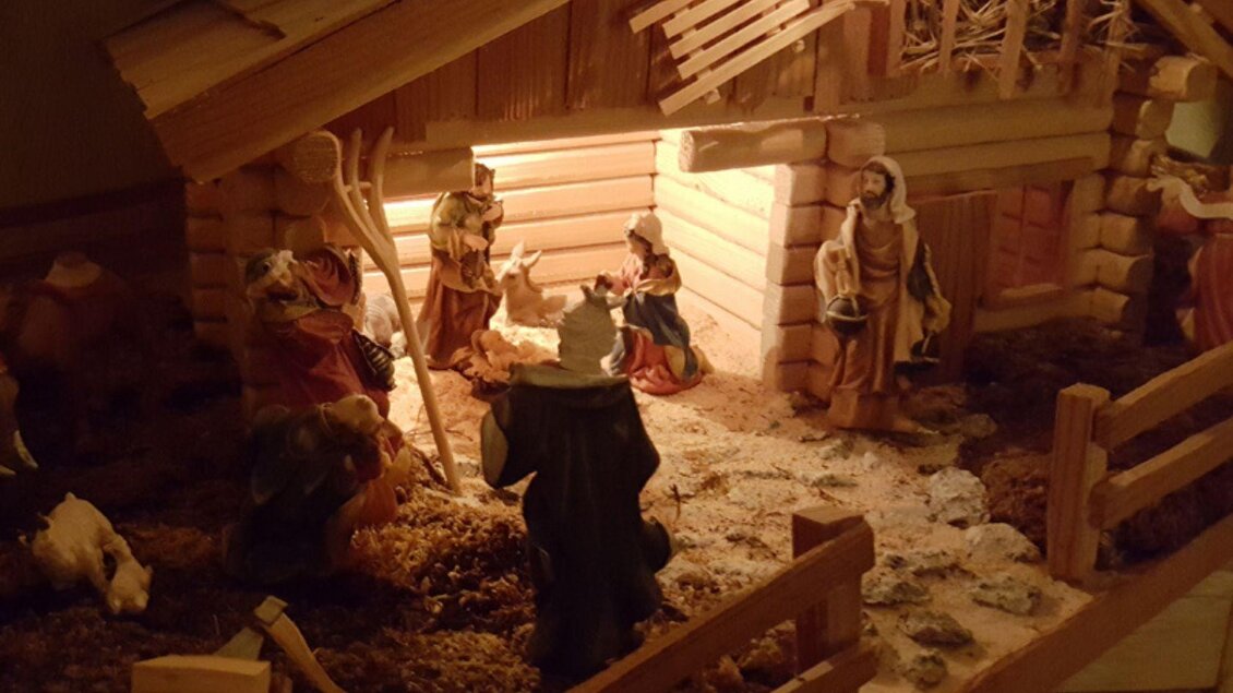 Eine Weihnachtskrippe mit Figuren, die die Geburt Jesu darstellen. Im Hintergrund ist ein beleuchteter Stall zu sehen, umgeben von Tieren. | © Michaela Geistberger