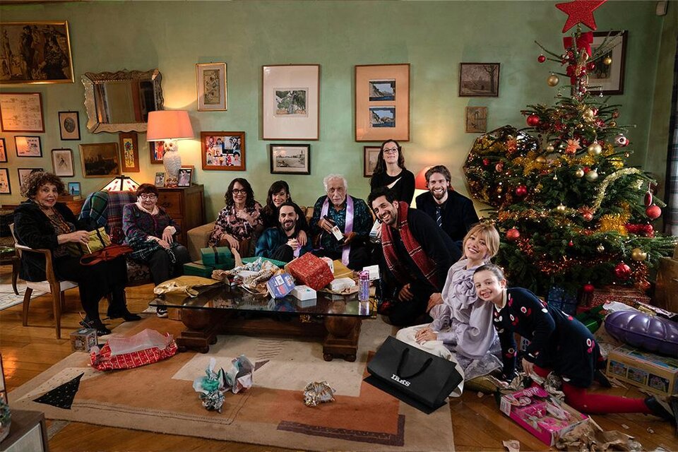 Eine fröhliche Familie sitzt in einem festlich dekorierten Raum um einen geschmückten Weihnachtsbaum. Geschenke liegen auf dem Tisch und der Stimmung ist gemeinsam feierlich. | ©  Luna Film