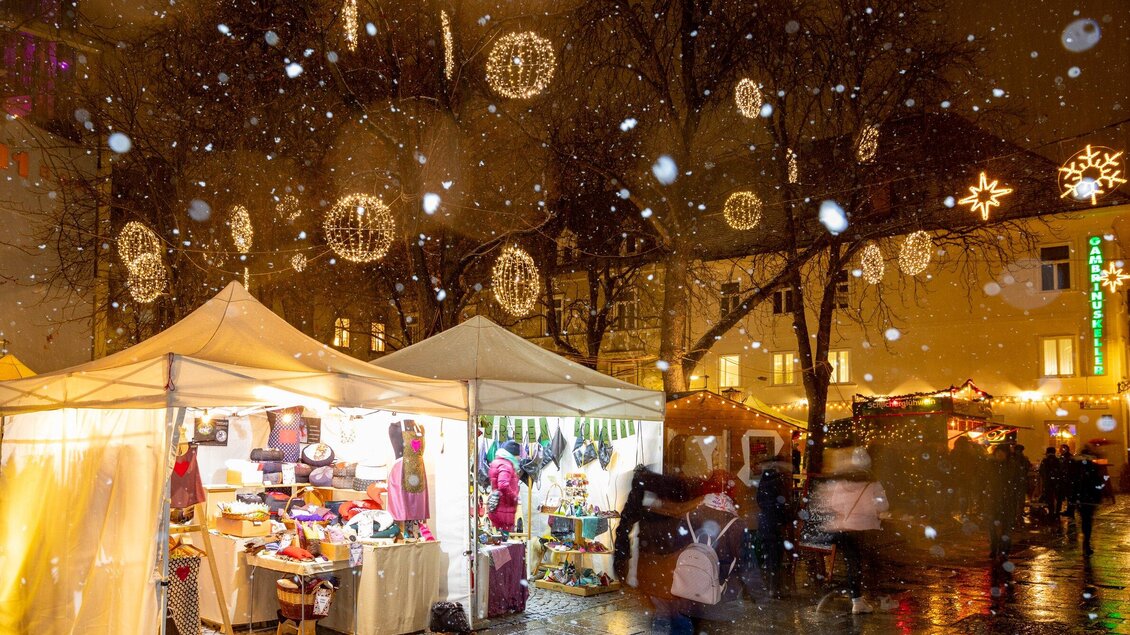 Ein festlicher Weihnachtsmarkt mit stimmungsvoller Beleuchtung und geschmückten Ständen. Es schneit leicht, und die Atmosphäre ist festlich und einladend. | © Graz Tourismus-Harry Schiffer