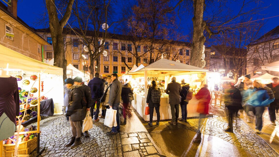 Ein abendlicher Markt mit bunten Ständen und Besuchern. Die Atmosphäre ist lebhaft und einladend unter den Lichtern der Bäume. | © Graz Tourismus - Harry Schiffer