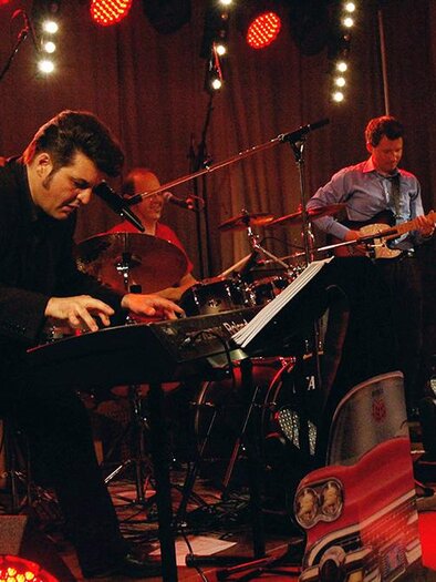 A band performs live. The musician plays the piano while other band members play the drums and guitar. | © Sigrid Querch