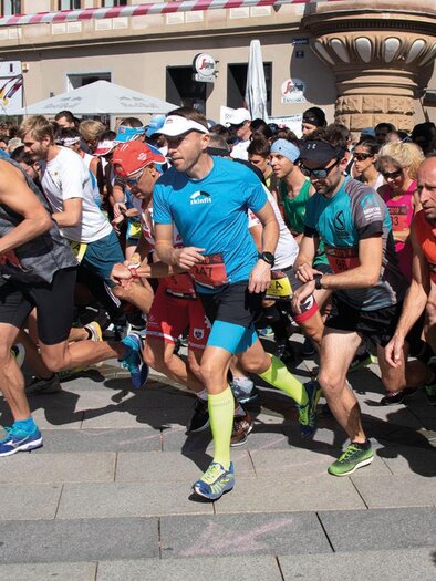A group of runners starts a race on a busy street. The athletes are wearing various sports outfits and show a lot of energy. | © Pressberger