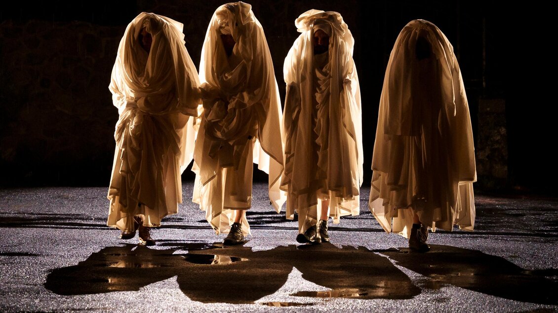 Vier Personen in eleganten, langen Gewändern stehen im Dunkeln. Ihre Silhouetten werfen interessante Schatten auf den Boden. | © c_Vincent