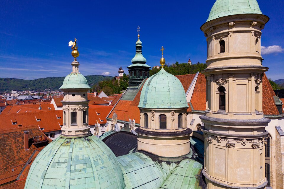 Eine beeindruckende Stadtansicht mit historischen Gebäuden und grünen Kuppeln. Der klare Himmel und die roten Dächer verleihen der Szene einen besonderen Charme. | © Graz Tourismus-Harry Schiffer