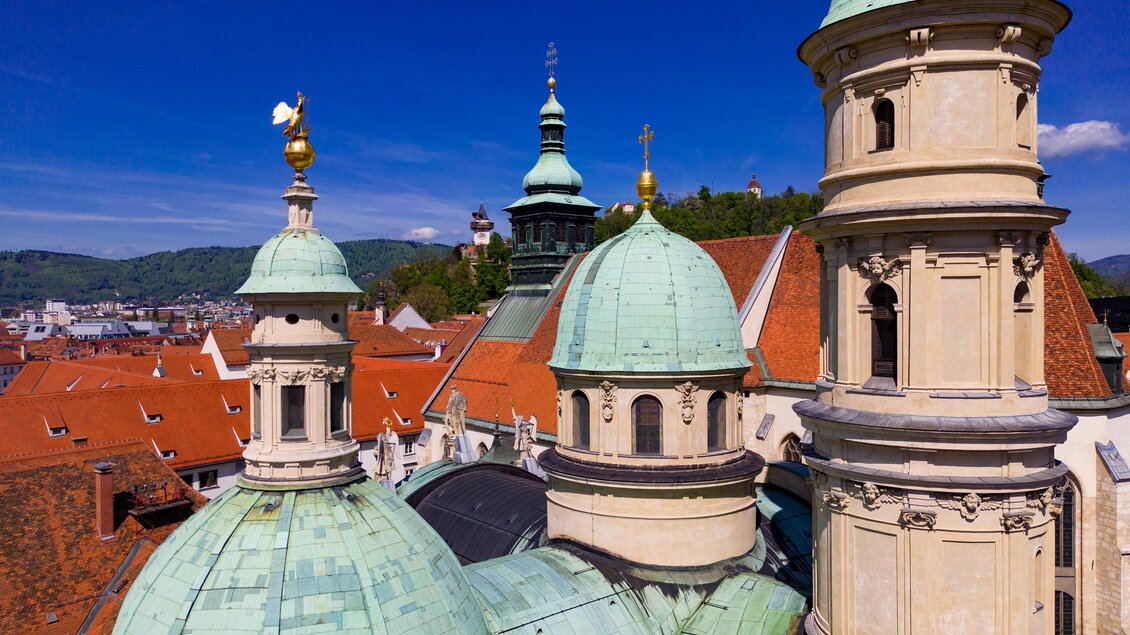 Eine beeindruckende Stadtansicht mit historischen Gebäuden und grünen Kuppeln. Der klare Himmel und die roten Dächer verleihen der Szene einen besonderen Charme. | © Graz Tourismus-Harry Schiffer
