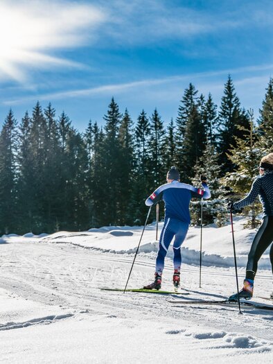 Ein Mann und eine Frau skaten auf der frisch präparierten Langlaufloipe auf der Hebalm, bei Sonnenschein und Neuschnee.  | © Region Graz-Mias Photoart