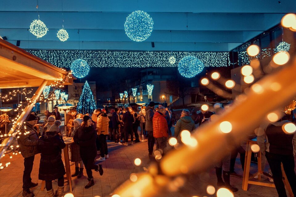 Ein festlicher Weihnachtsmarkt mit bunten Lichtern und vielen Menschen. Über dem Markt hängen funkelnde Dekorationen, die eine fröhliche Atmosphäre schaffen. | © MG Lannach - Petru Rimovetz