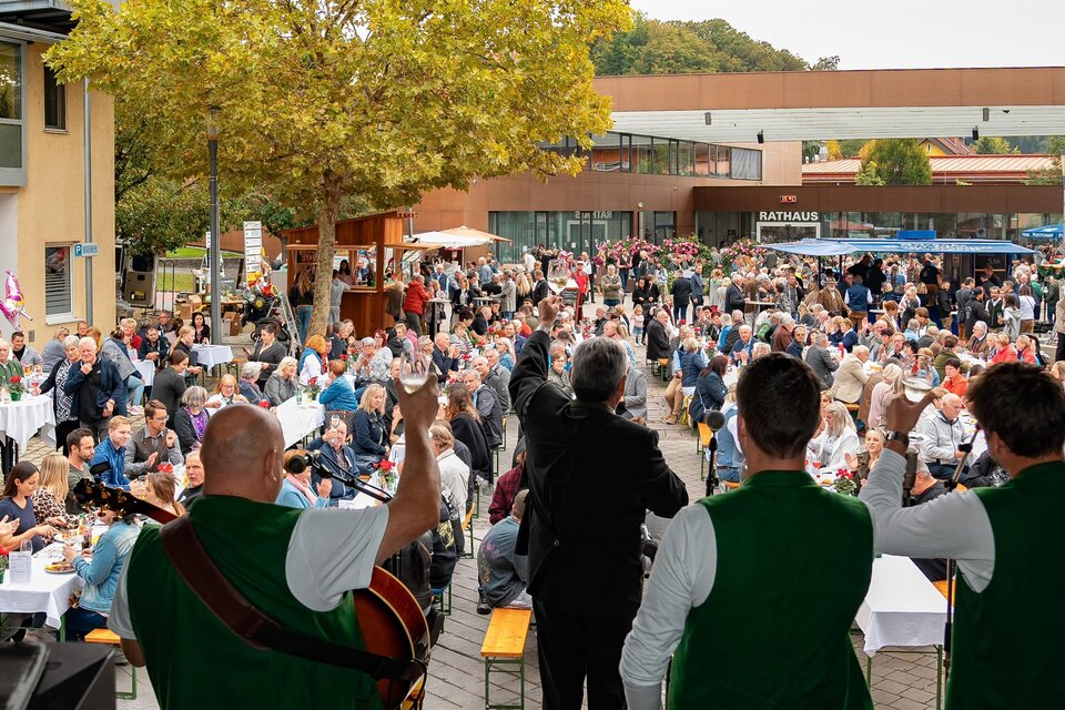 Eine lebhafte Veranstaltung mit vielen Menschen, die an Tischen sitzen und sich unterhalten. Im Vordergrund spielen Musiker in traditionellen Outfits. | © MG Lannach - Petru Rimovetz