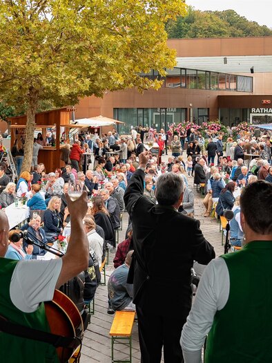 A lively event with many people sitting at tables and chatting. In the foreground, musicians are performing in traditional outfits. | © MG Lannach - Petru Rimovetz