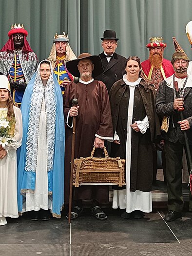 A group of people in traditional clothing stands on a stage. They smile and pose for the photo while portraying various historical or festive characters. | © Tv Murau