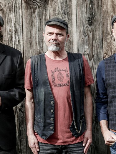 Three men are standing in front of a wooden wall. They are wearing casual clothing and hats. | © Laube-Schober-Kainz