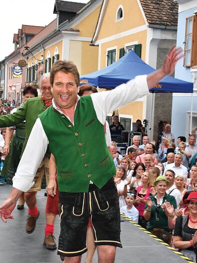 A lively festival event with many spectators on the street. A man in traditional costume is dancing and attracting attention. | © Hiden-Wagner
