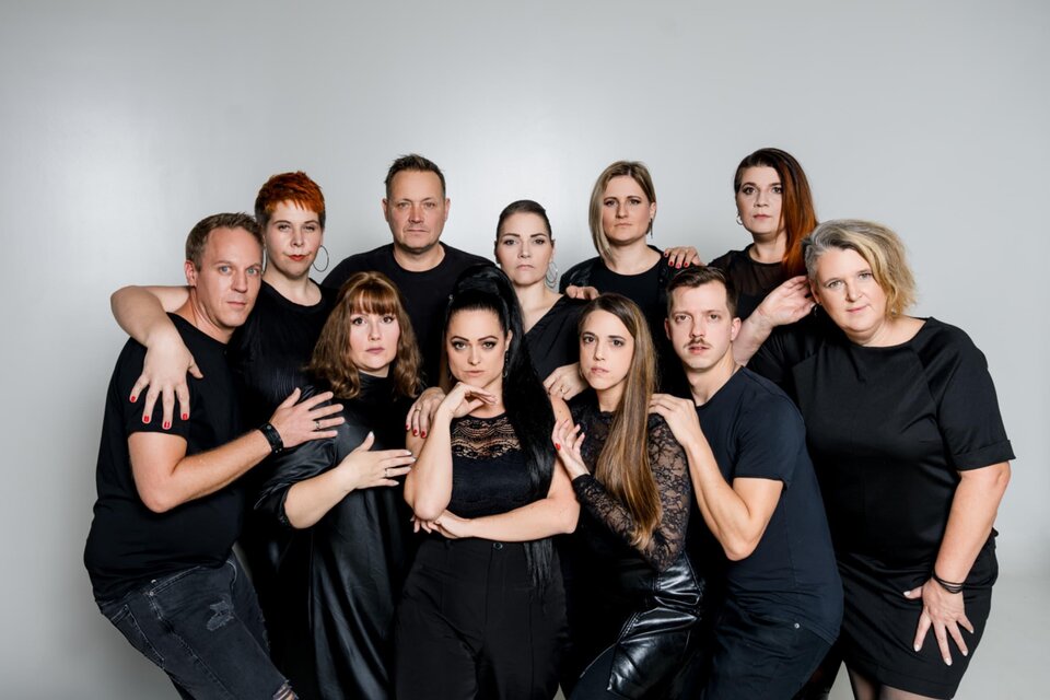 Eine Gruppe von Personen steht zusammengestellt in eleganter schwarzer Kleidung. Sie posieren vor einem neutralen Hintergrund, ausdrucksstark und vielfältig in ihrer Präsenz. | © Michaela Lorber