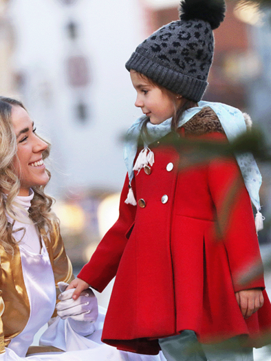 A smiling girl in a red coat is speaking with a woman in a golden costume. The scene takes place in a festive setting. | ©  Katharina Wassler