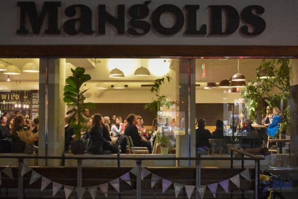 Ein lebhaftes Restaurant namens Mangolds mit zahlreichen Gästen. Die Innenräume sind modern gestaltet und mit Pflanzen dekoriert. | © Jaqueline-Scheiber