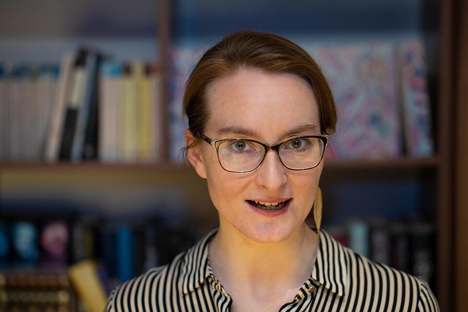 Eine Frau mit Brille steht vor einem Bücherregal. Sie trägt ein gestreiftes Hemd und schaut direkt in die Kamera. | ©  Gerald Schutting