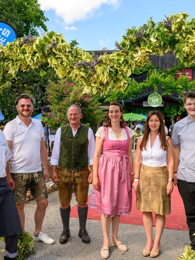 A group of people stands in front of a festively decorated entrance. The individuals are wearing traditional clothing and smiling at the camera. | © ©pixelmaker