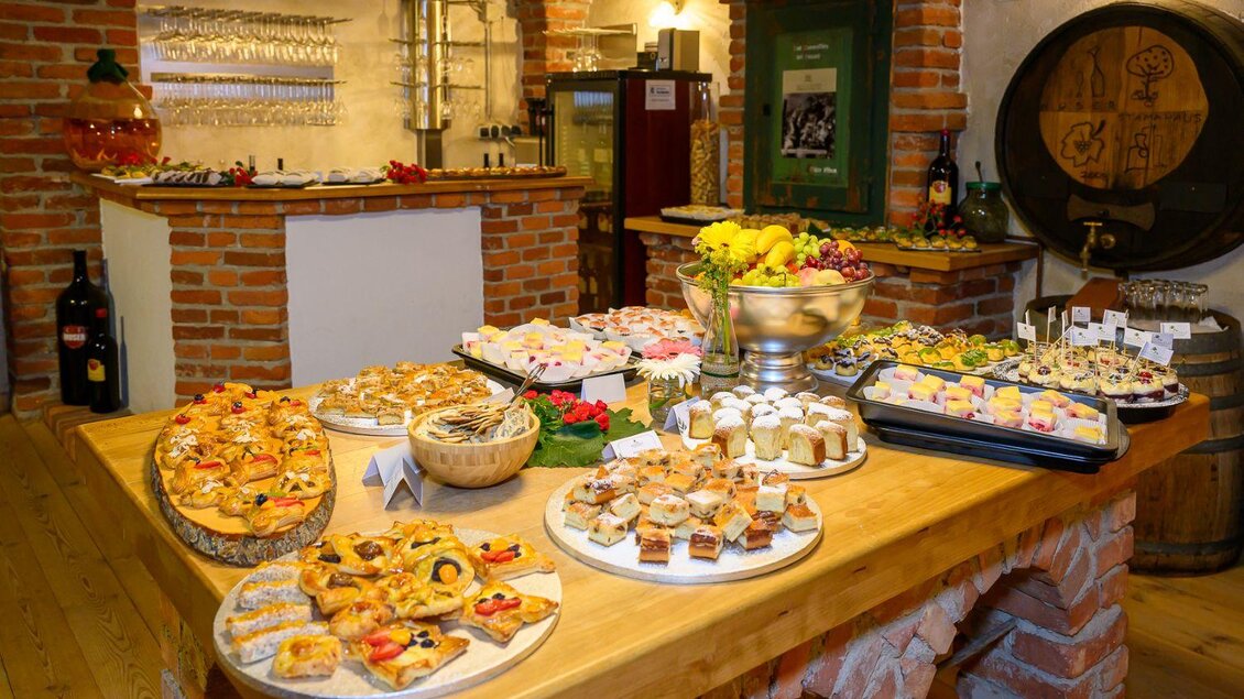Ein ansprechend gedeckter Tisch mit einer Vielzahl von süßen und herzhaften Leckereien. Im Hintergrund sind Steinelemente und eine Bar zu sehen. | © ©pixelmaker
