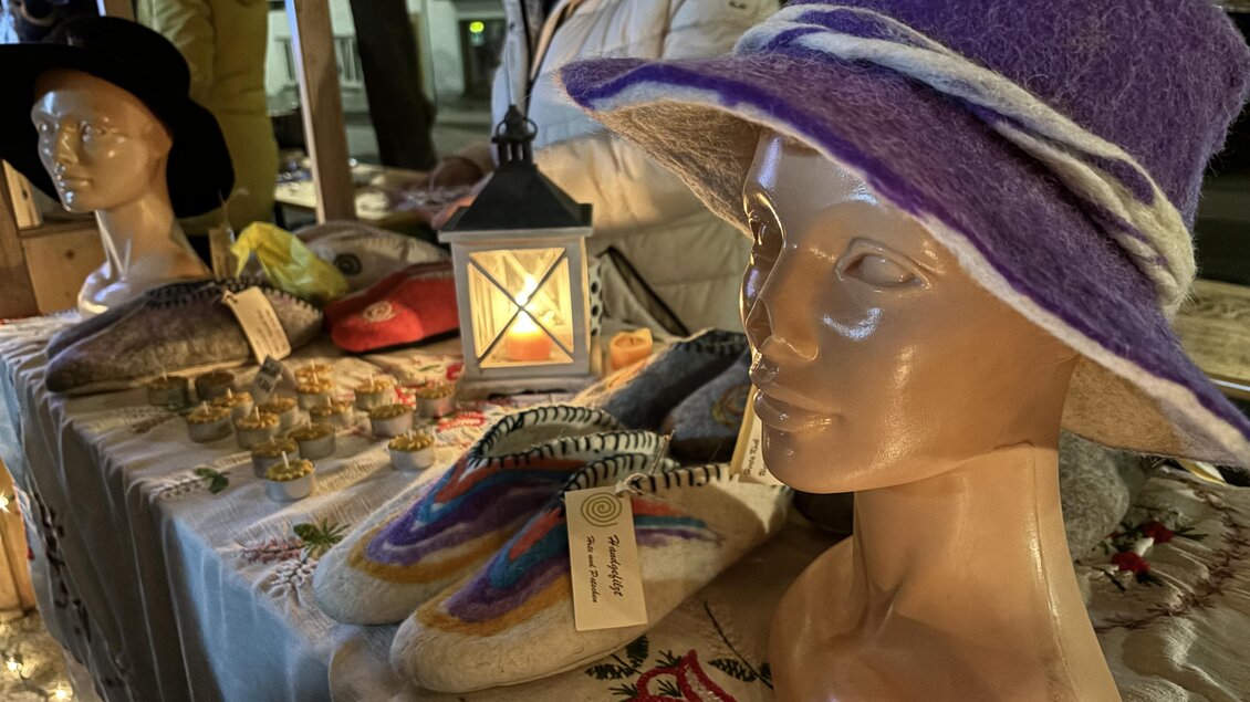 Ein Stand mit handgefertigten Produkten, darunter Filzhüte und Hausschuhe. Im Hintergrund steht eine Laterne und eine Person ist zu sehen. | © Oststeiermark Tourismus