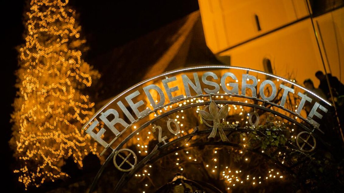 Eine festliche Szene mit einem leuchtenden Eingang zur "Friedensgrotte". Im Hintergrund steht ein geschmückter Weihnachtsbaum. | © Joachim Otter