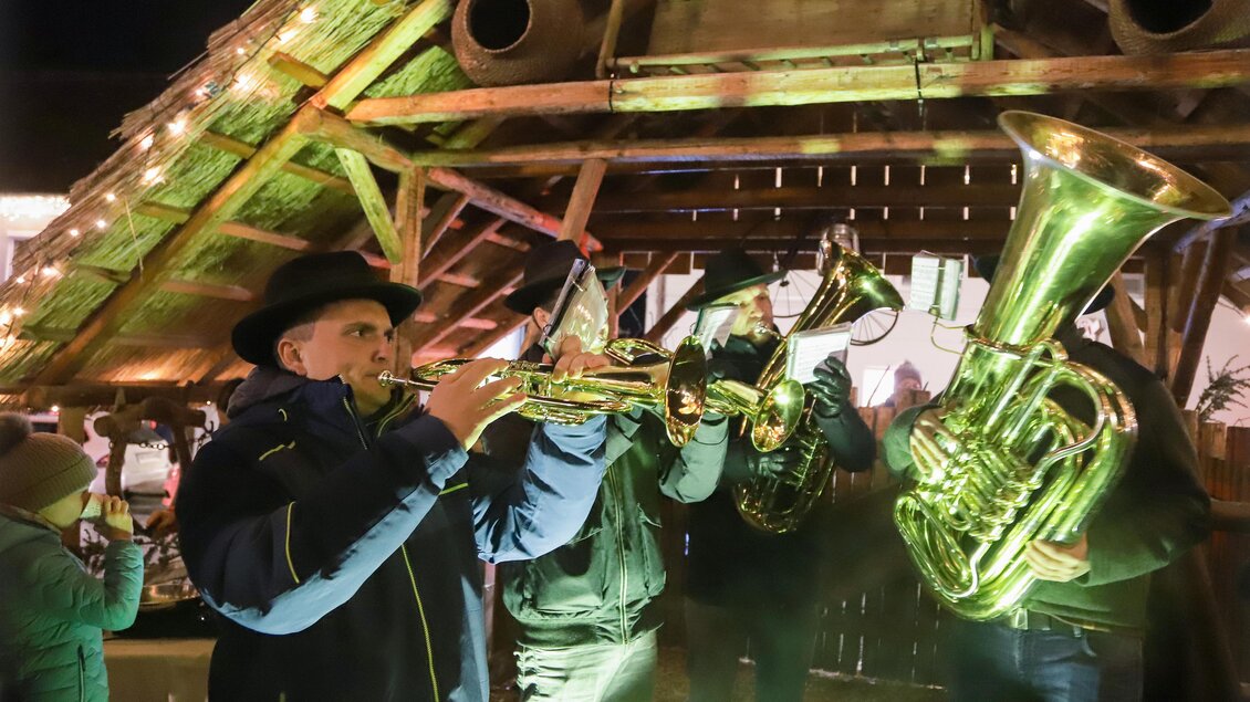 Eine Gruppe von Musikern spielt unter einem Holzdach. Sie haben verschiedene Blasinstrumente und treten in einer festlichen Atmosphäre auf. | © Iris Bloder
