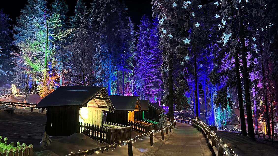 Ein winterlicher Weg, umgeben von beleuchteten Bäumen und kleinen Hütten. Die Szene strahlt eine festliche Stimmung mit bunten Lichtern aus. | © Anna-Lena König