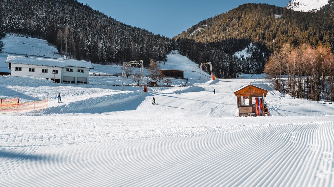 Eine winterliche Landschaft mit schneebedeckten Bergen und einem Skilift. Im Vordergrund sind die präparierte Piste und eine kleine Hütte zu sehen. | © Christoph Lukas