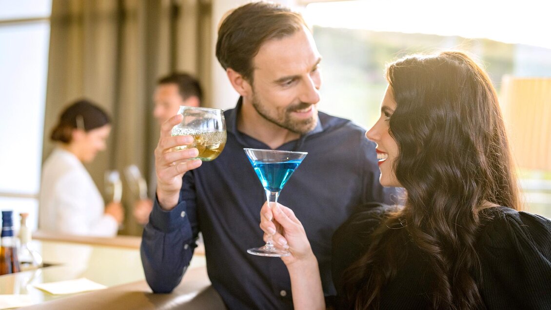 Ein Paar genießt Drinks in einer stilvollen Bar. Sie lachen und stoßen mit ihren Gläsern an.