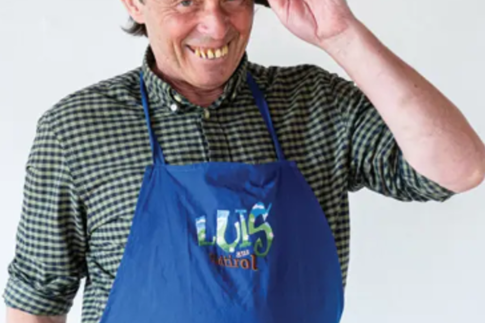 Ein lächelnder Mann trägt einen Trachtenhut und eine blaue Schürze. Er scheint freundlich und einladend zu sein. | © Luis aus Südtirol