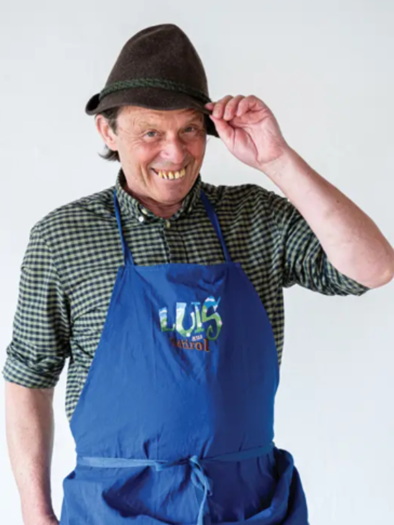 A smiling man is wearing a traditional hat and a blue apron. He seems friendly and welcoming. | © Luis aus Südtirol